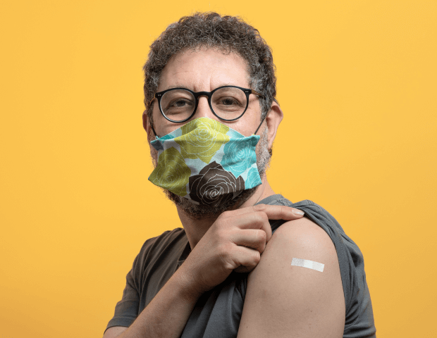 An older man wearing a mask and showing off his vaccination bandaid